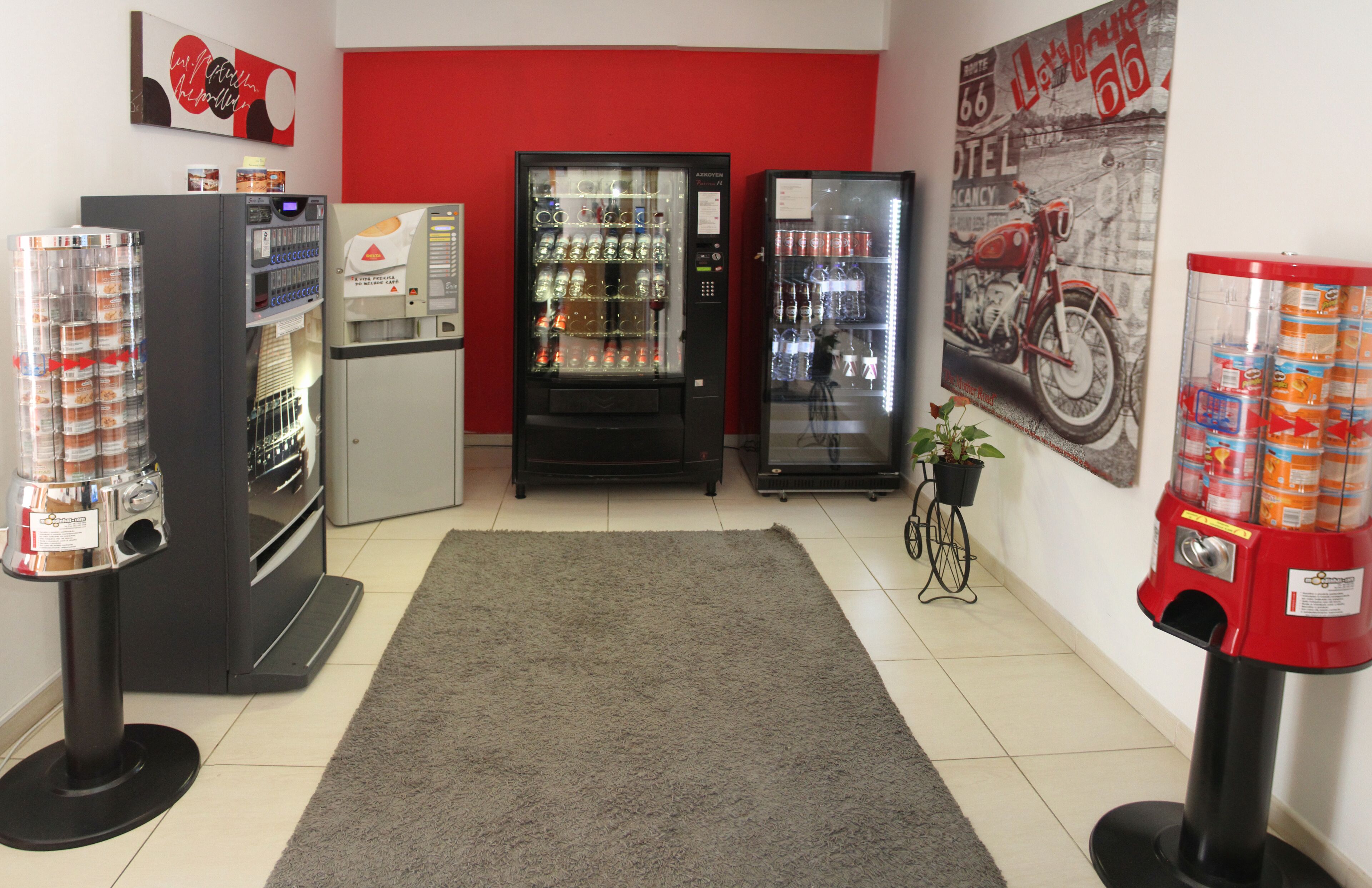 A room with vending machines, a refrigerator, and a motorcycle-themed wall.