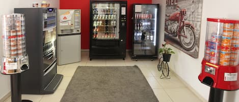 A room with vending machines, a refrigerator, and a motorcycle-themed wall.