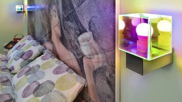 Una cama con ropa de cama de lunares coloridos, una lámpara de pared y un cuadro abstracto grande.