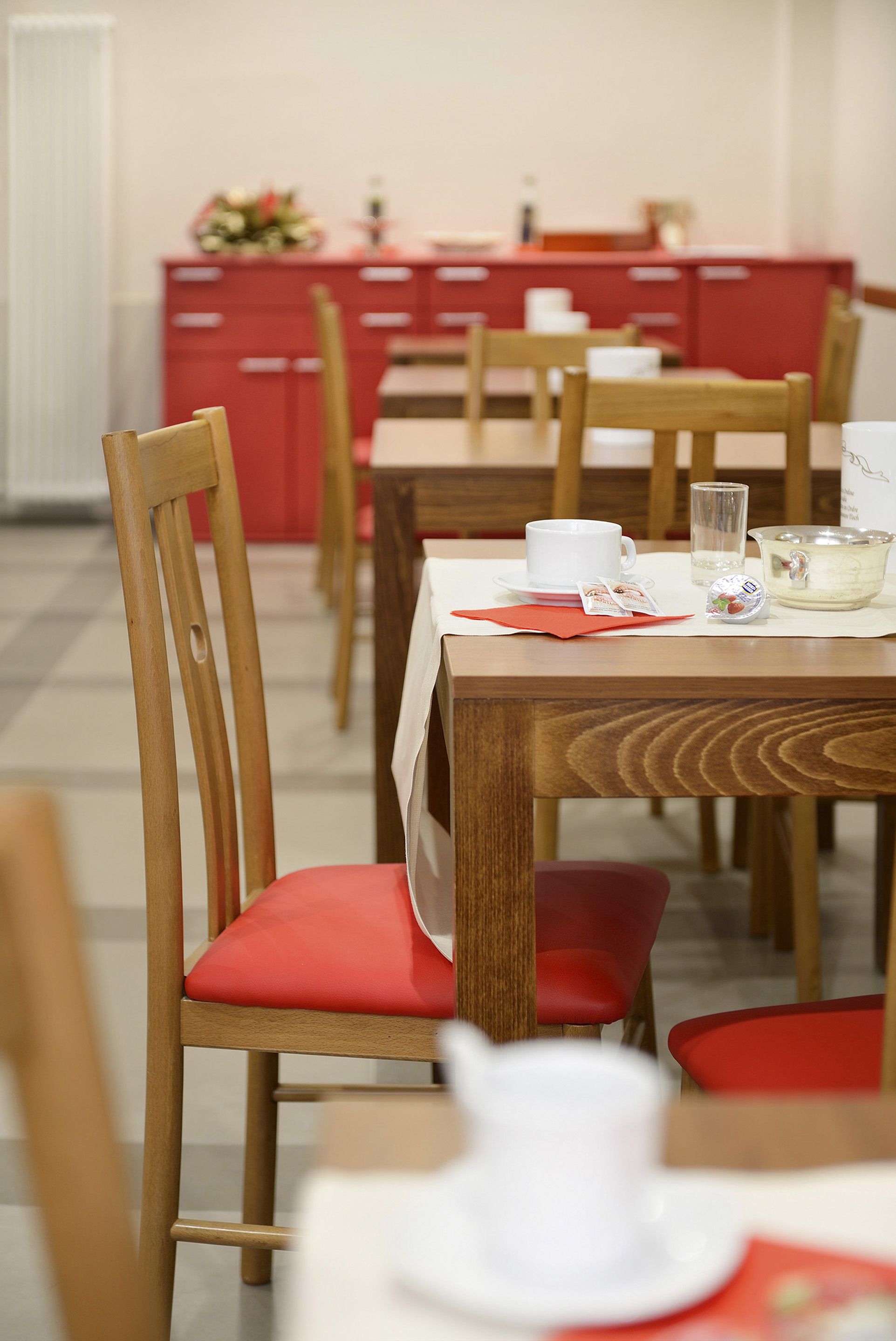 A dining area with wooden chairs and tables, a red cabinet in the background, and a white teapot on the table.