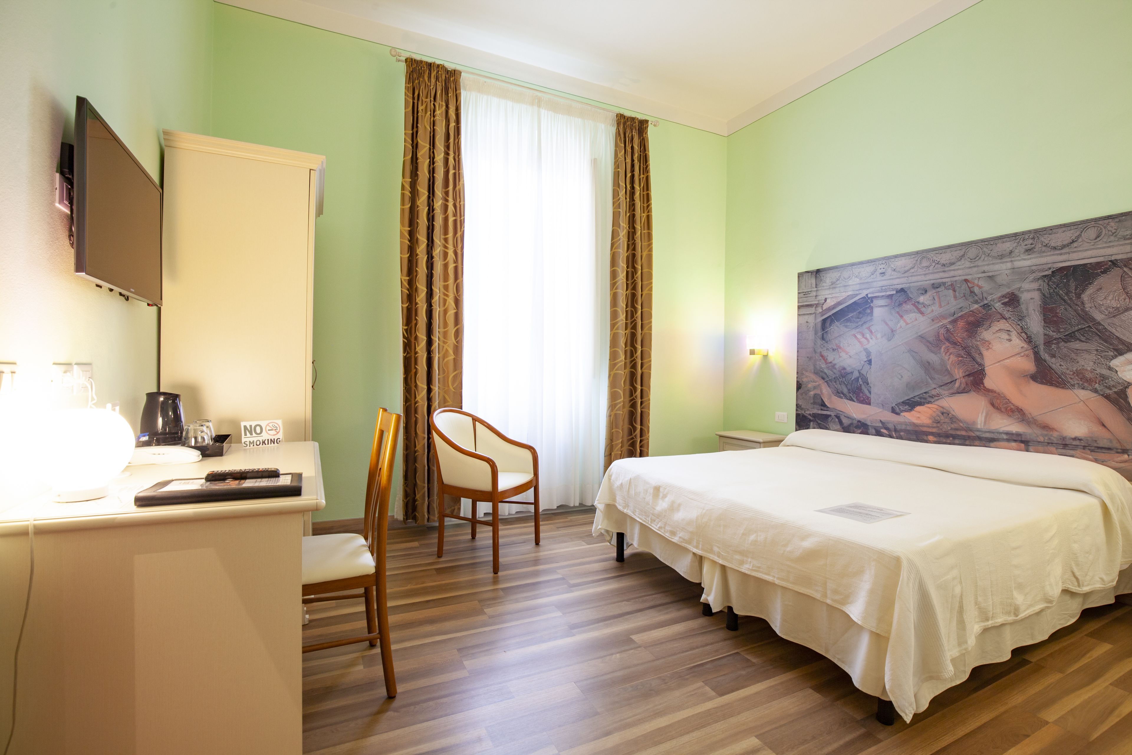 Habitación de hotel con cama, un escritorio con silla, televisor y un cuadro en la pared.