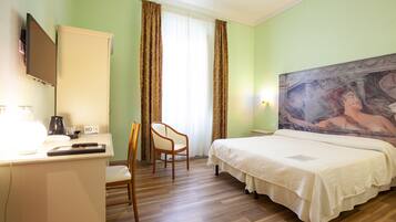 Habitación de hotel con cama, un escritorio con silla, televisor y un cuadro en la pared.
