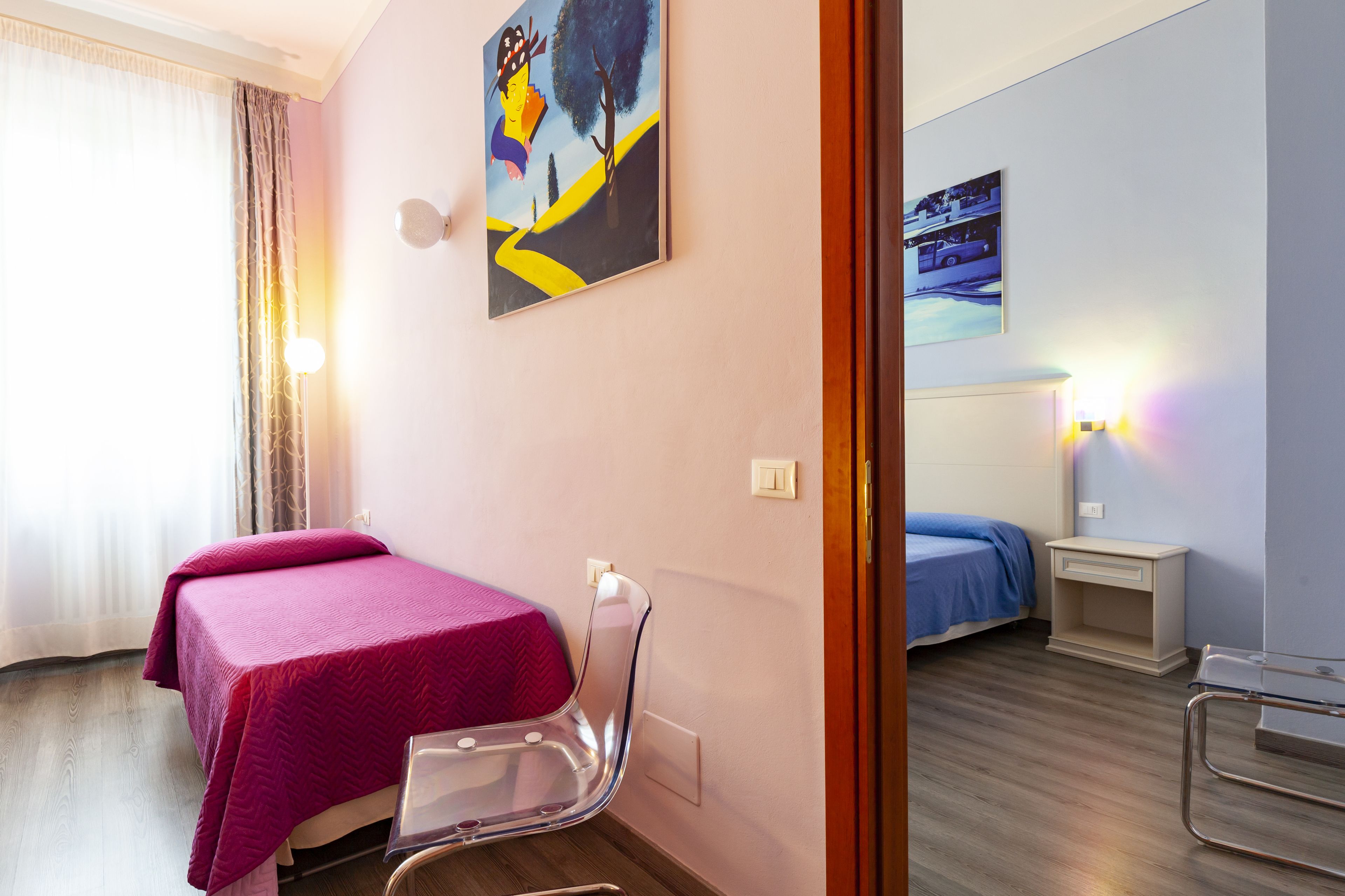 A hotel room with two beds, a chair, a nightstand, and wall art.