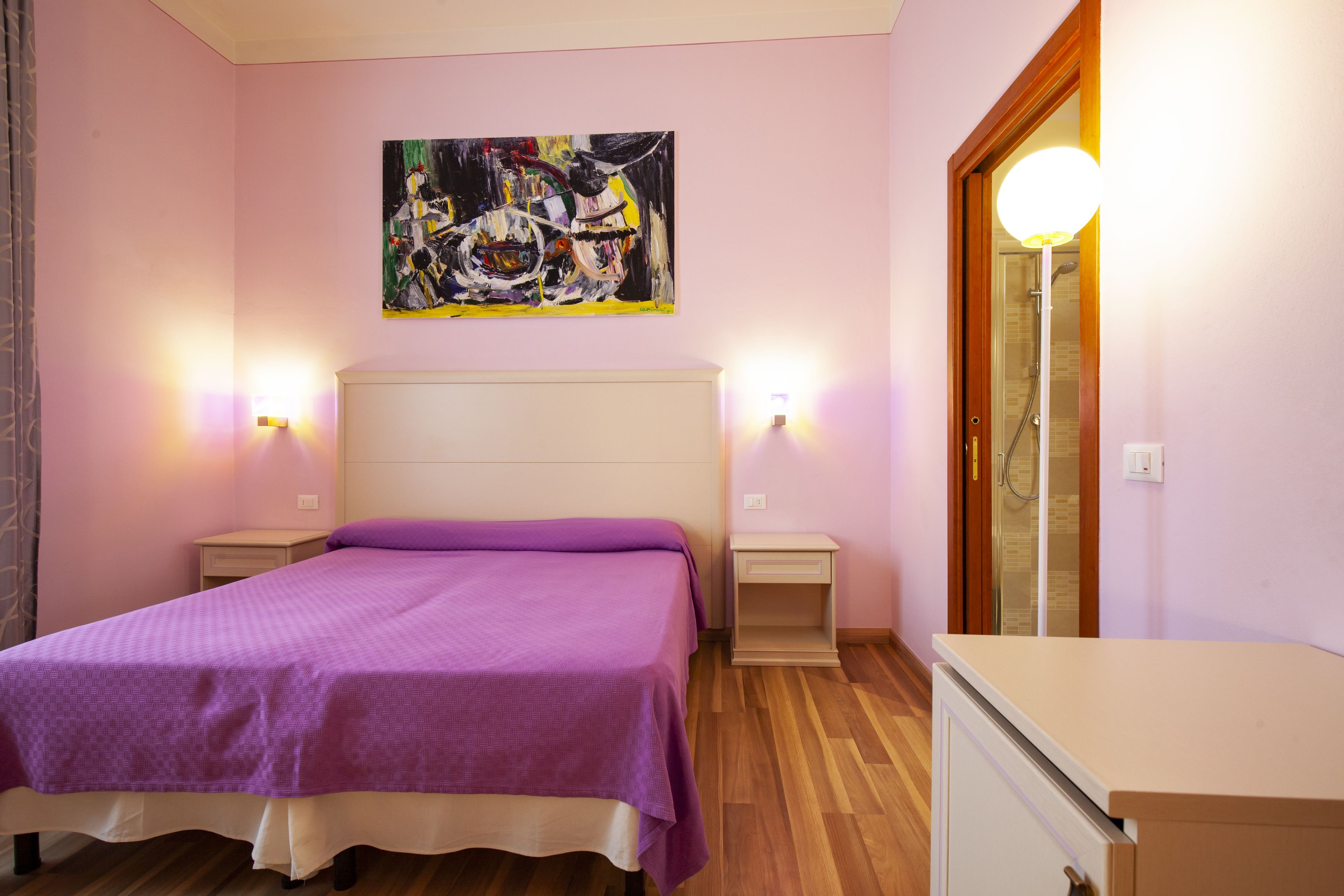 A bedroom with a bed, nightstands, a dresser, a painting, and a bathroom door.