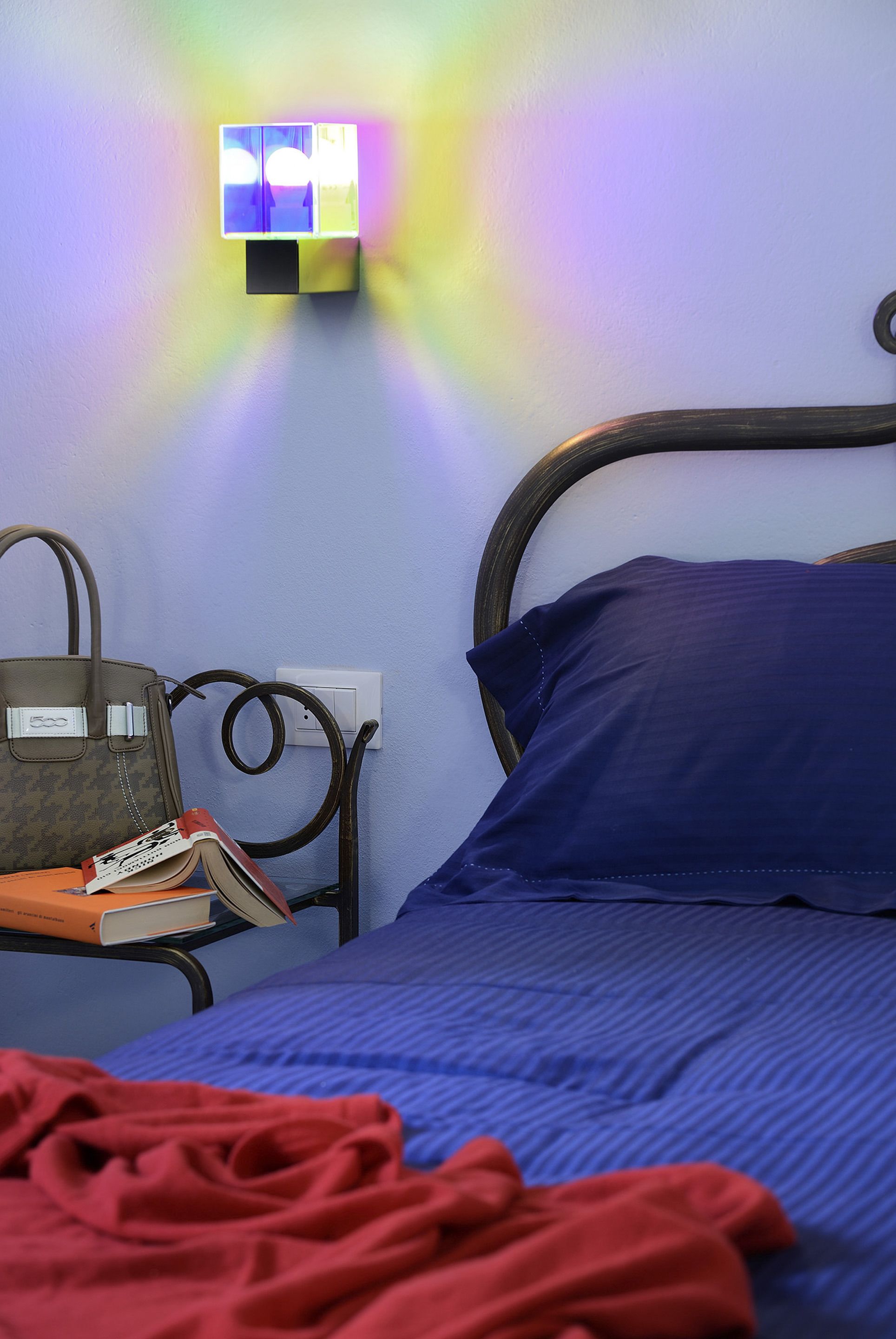 A room with a bed, a nightstand, a lamp, and a wall-mounted light fixture.