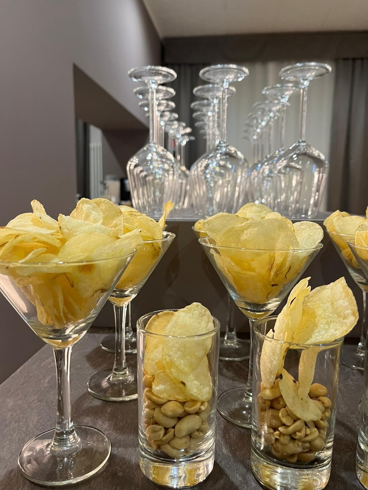 Una mesa con vasos de vidrio transparente que contienen papas fritas y cacahuates.