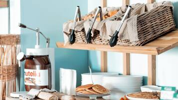 A breakfast buffet with various pastries, a jar of Nutella, and utensils on a wooden counter.