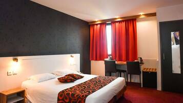 A hotel room with a bed, a desk, two chairs, a small table, and a wardrobe.