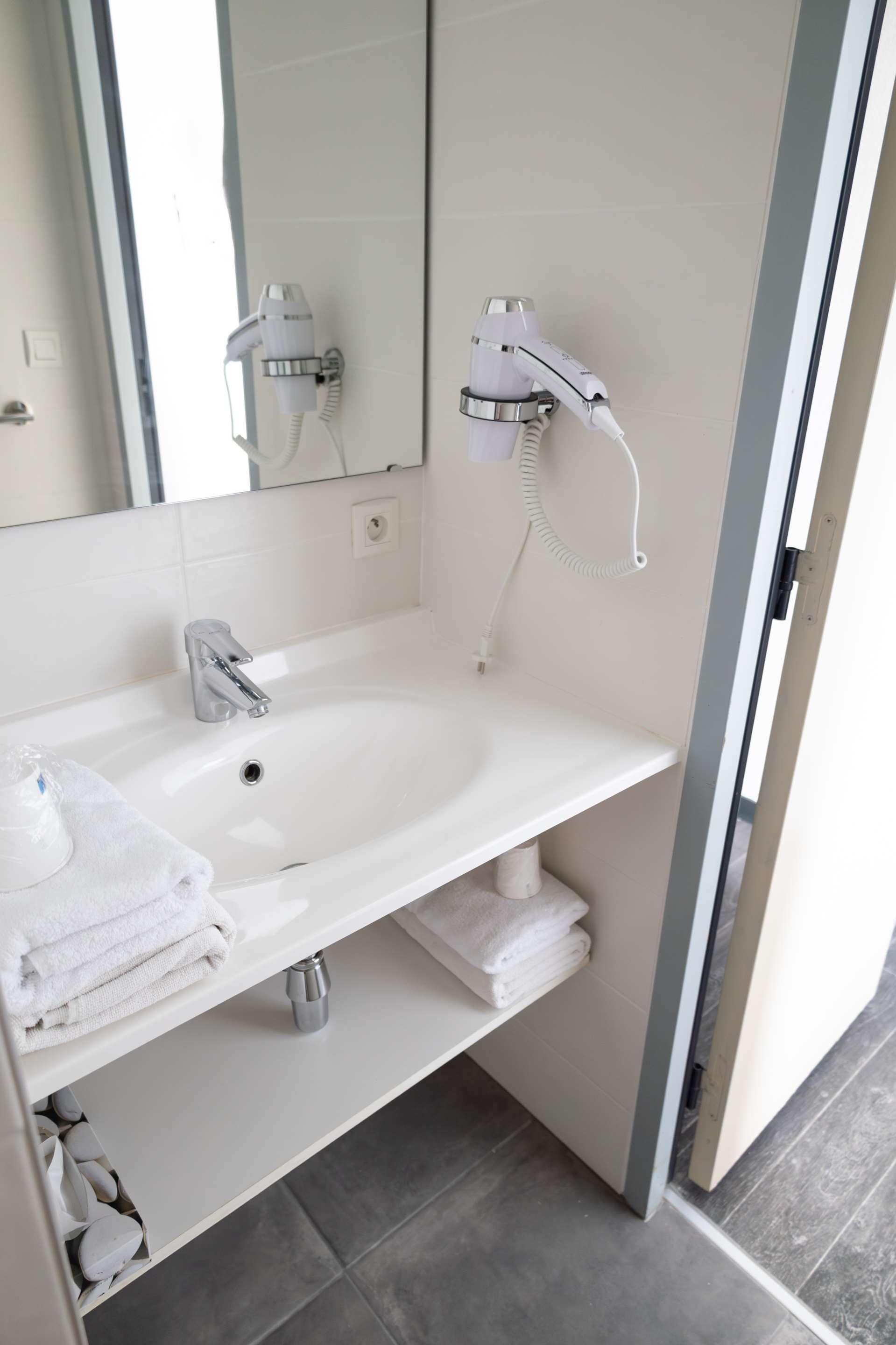 A bathroom with a white sink, a mirror, a hairdryer, and a towel rack.
