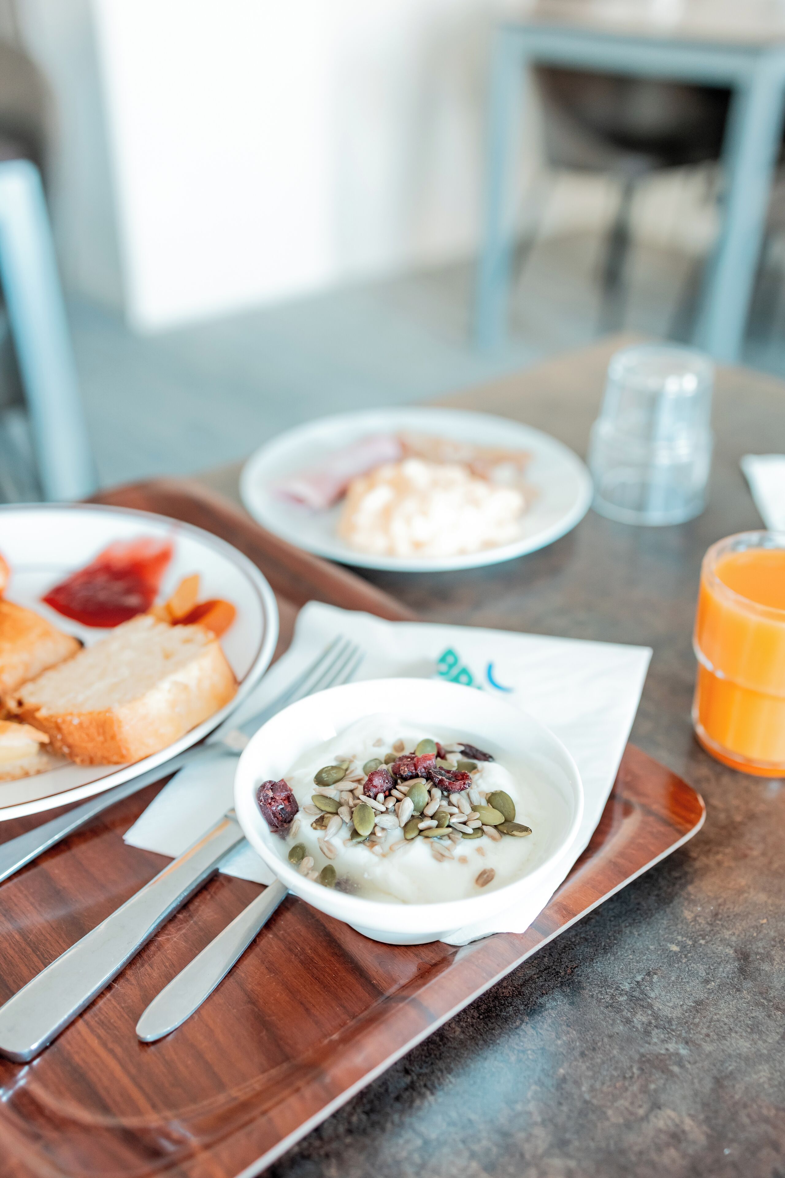 A breakfast setting with a plate of toast, a bowl of yogurt with seeds, and a glass of orange juice on a wooden tray.