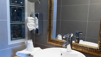 A modern bathroom with a large white sink, a mirror with a decorative frame, a towel dispenser, and a window with frosted glass panels.