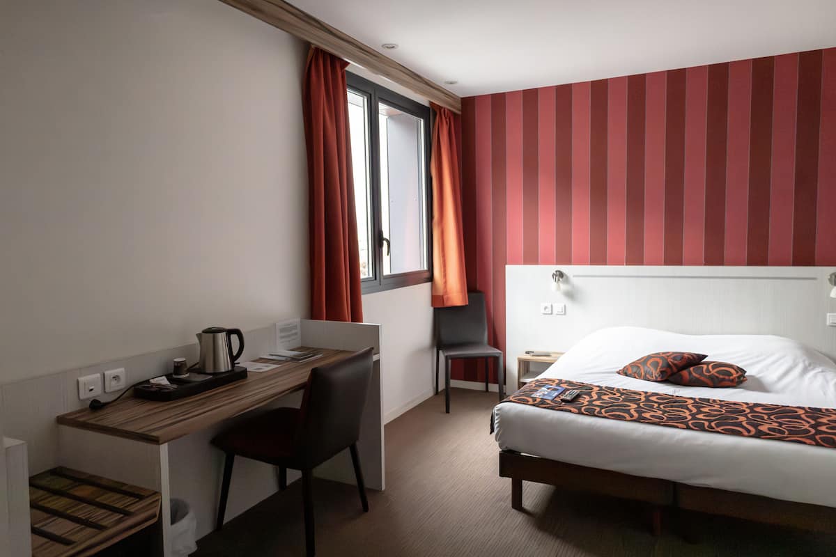 A hotel room with a bed, a desk, a chair, and a window with curtains.