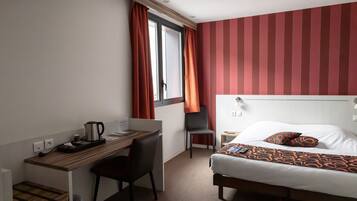 A hotel room with a bed, a desk, a chair, and a window with curtains.