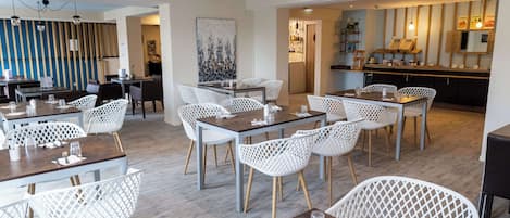A modern dining area with white lattice chairs and wooden tables, a bar area with a counter, and a large abstract painting on the wall.