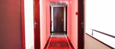 A hotel hallway with red carpet and wooden doors.