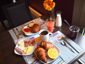 A breakfast table with croissants, orange juice, coffee, and a newspaper. - Hôtel Inn Design & Restaurant Vannes (Theix-Noyalo)