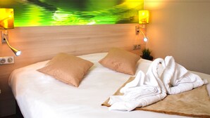 A hotel room with a bed, two pillows, a towel, a nightstand, a lamp, and a wall with a green and yellow design. - Hôtel Inn Design & Restaurant Vannes  (Theix-Noyalo)