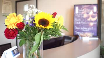 A reception desk with a vase of flowers, a framed menu, and a digital clock.