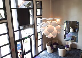 Un intérieur moderne avec de grandes fenêtres, un luminaire sphérique original et un espace salon avec des chaises blanches et violettes.