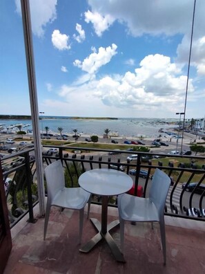 Un balcón con dos sillas y una mesa, con vista a una marina con barcos y una playa.