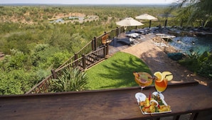 A deck with a pool, lounge chairs, and umbrellas overlooking a lush landscape. - Victoria Falls Safari Suites (Victoria Falls)