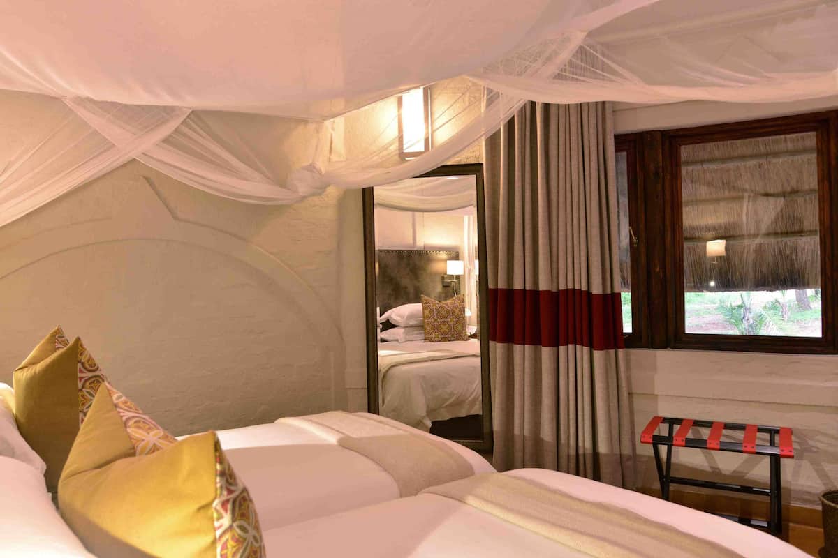 A bedroom with a canopy bed, a bedside table, a lamp, and a window with curtains.