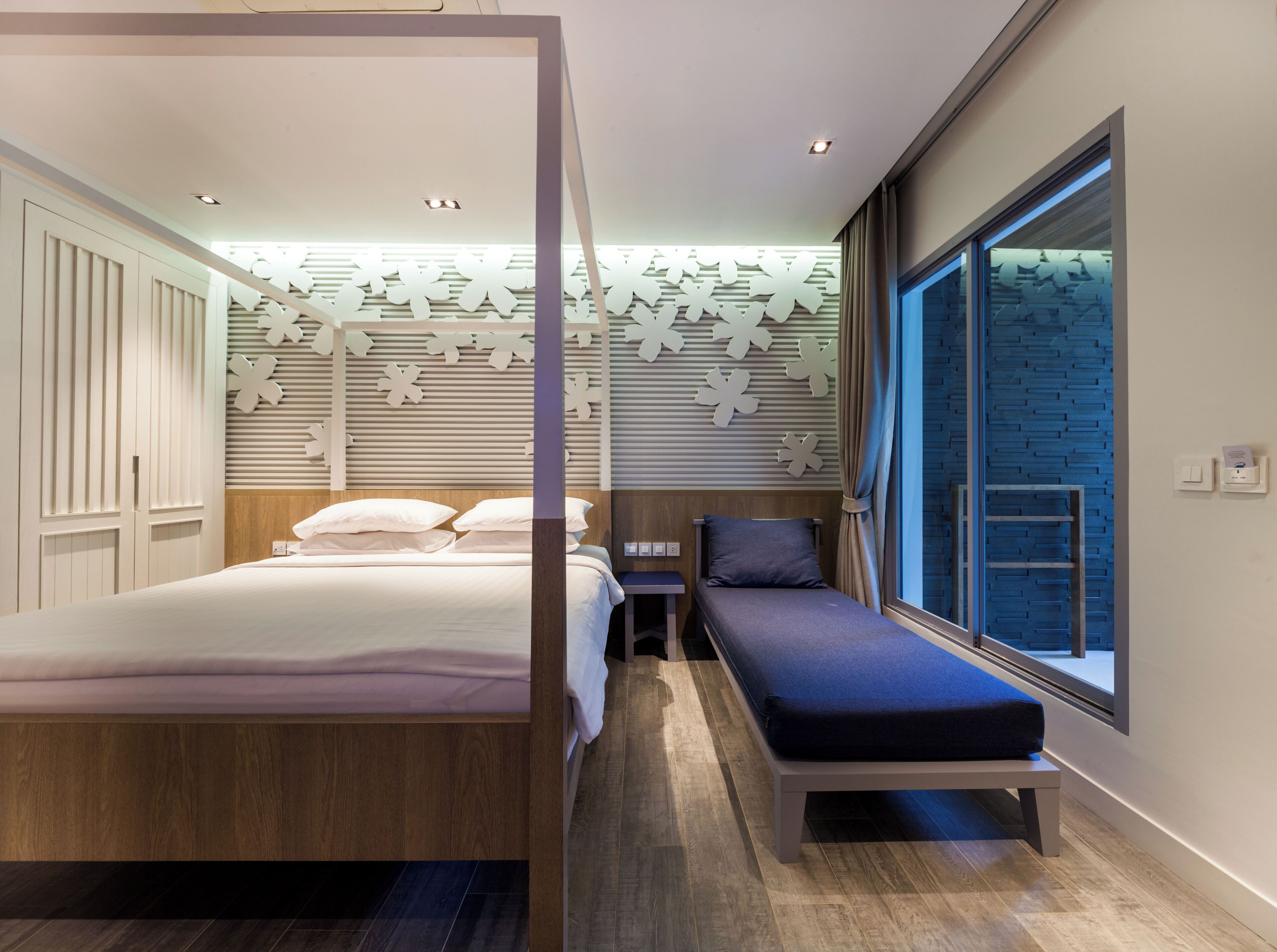 Ein modernes Schlafzimmer mit Bett, Nachttisch, Bank und großem Fenster.