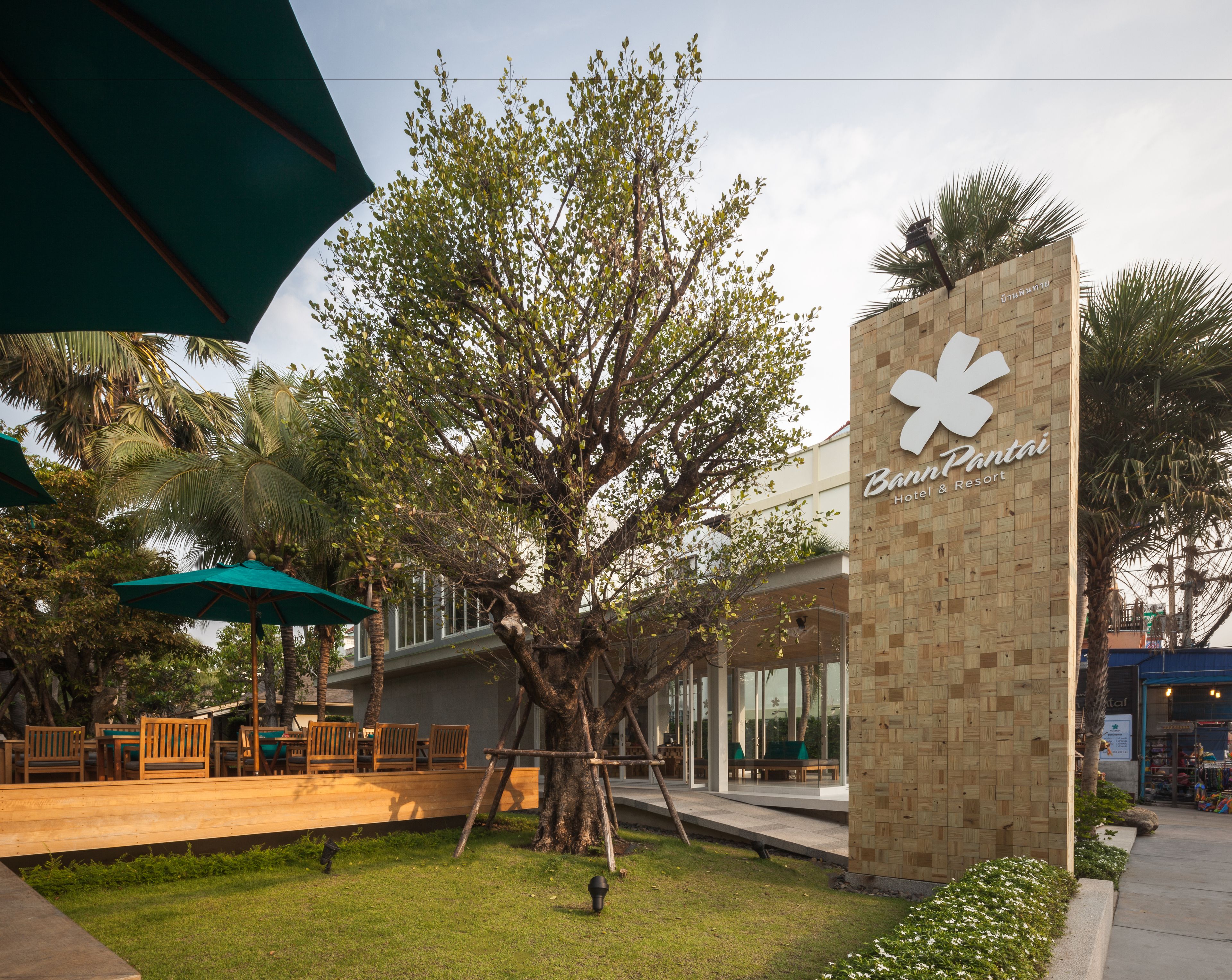 A Banni Pantai Hotel & Resort with a large tree in the foreground, outdoor seating area, and a signboard.