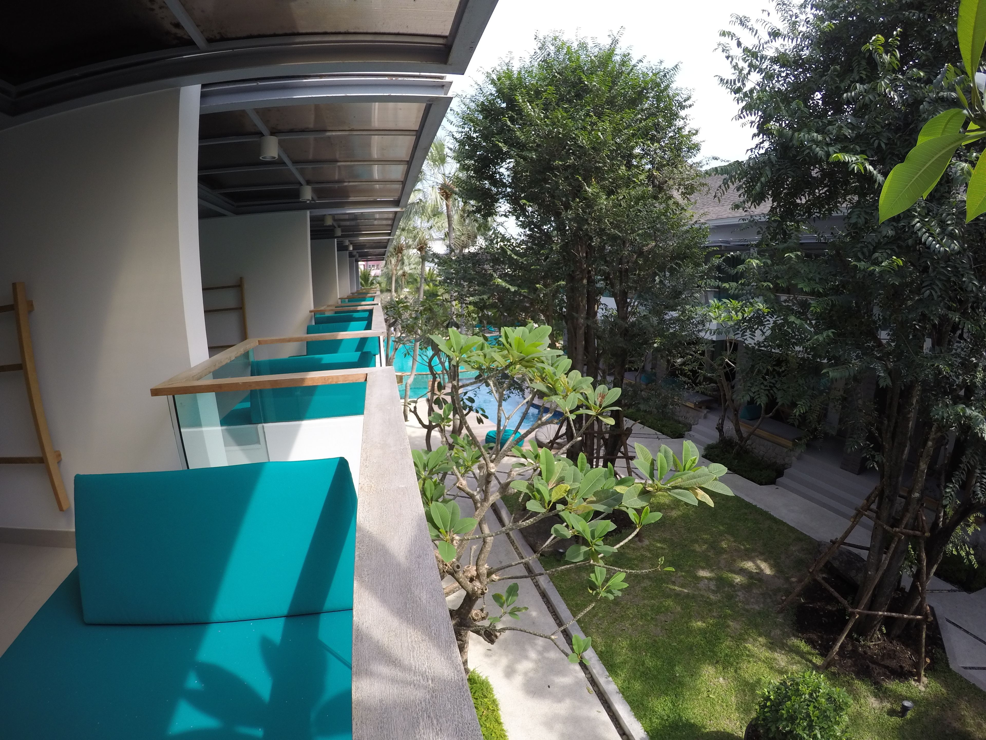 A corridor with teal cushioned seating, a pool, and surrounding greenery.