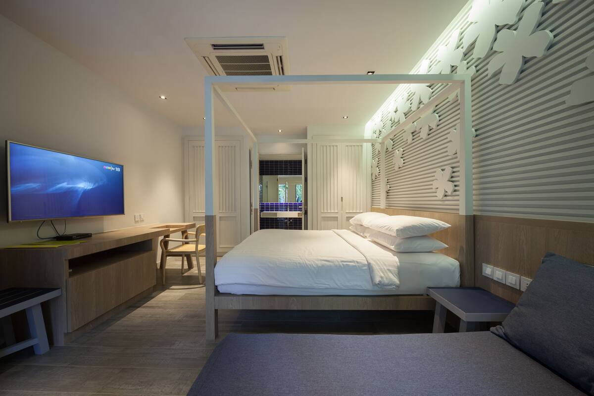 Une chambre d’hôtel moderne équipée d’un lit, d’un bureau, d’une télévision et d’une salle de bain visible à travers une porte ouverte.
