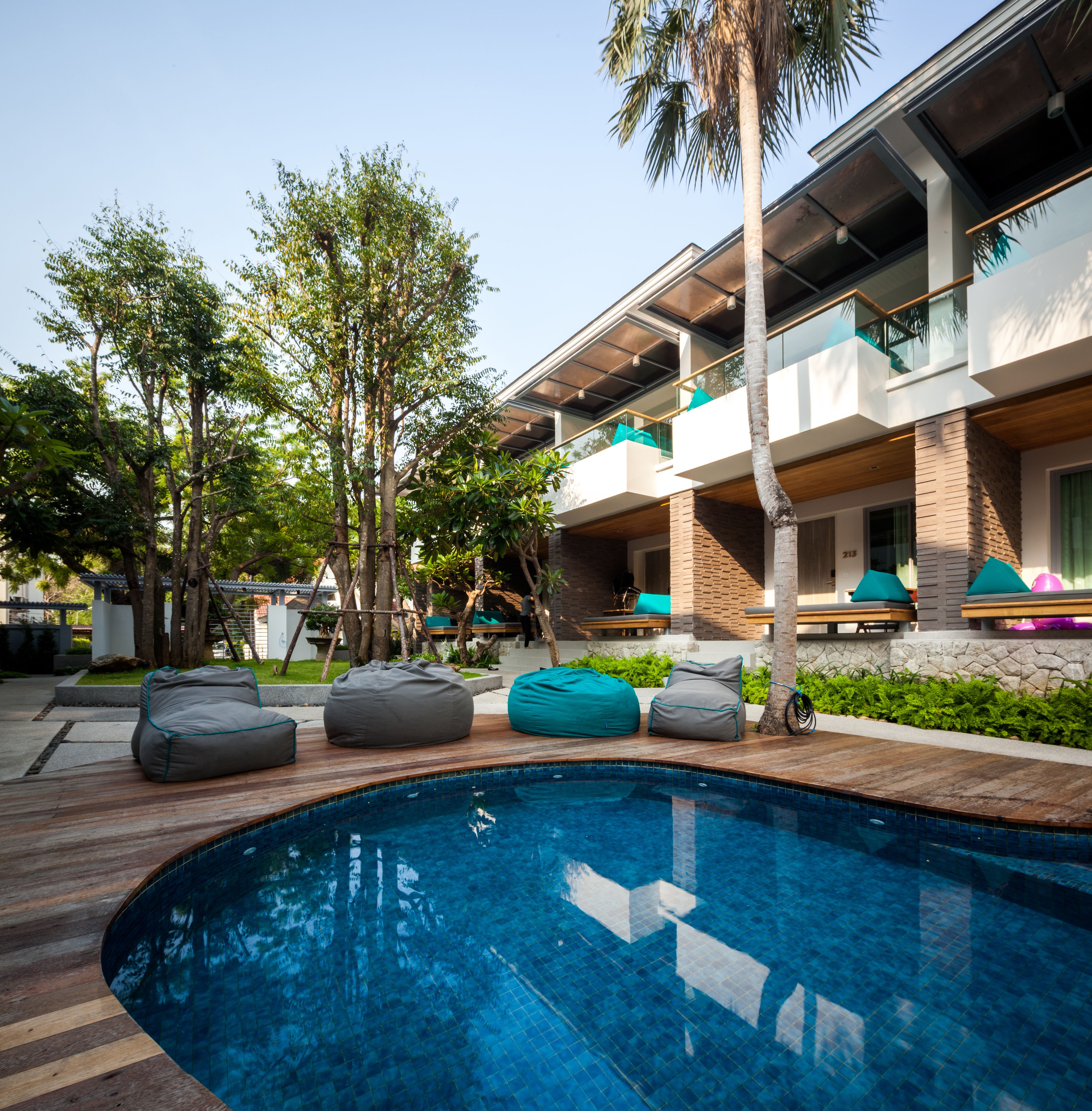 A modern outdoor pool area with a wooden deck, a swimming pool, and multiple seating areas including bean bags and lounge chairs.