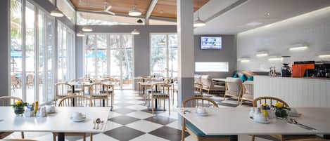 Un restaurante moderno con suelo a cuadros, sillas de madera y mesas preparadas para comer.