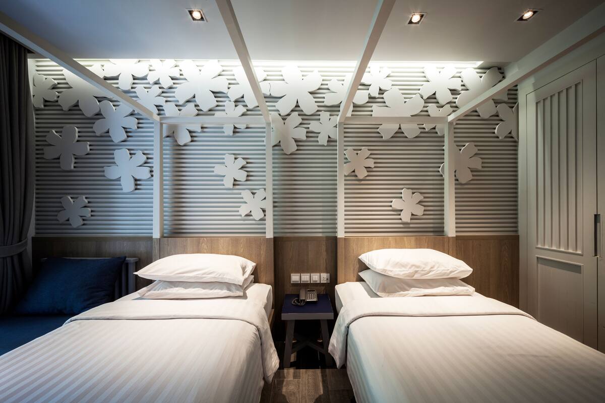Une chambre d’hôtel avec deux lits, une table de chevet et un mur décoratif orné de motifs découpés.