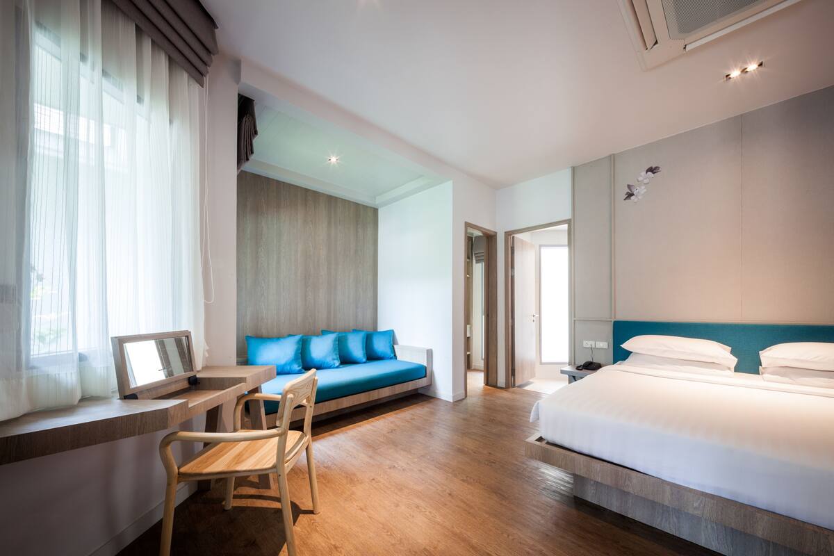 Une chambre d’hôtel moderne avec un plancher en bois, un canapé bleu, un bureau avec une chaise et un grand lit avec une literie blanche.