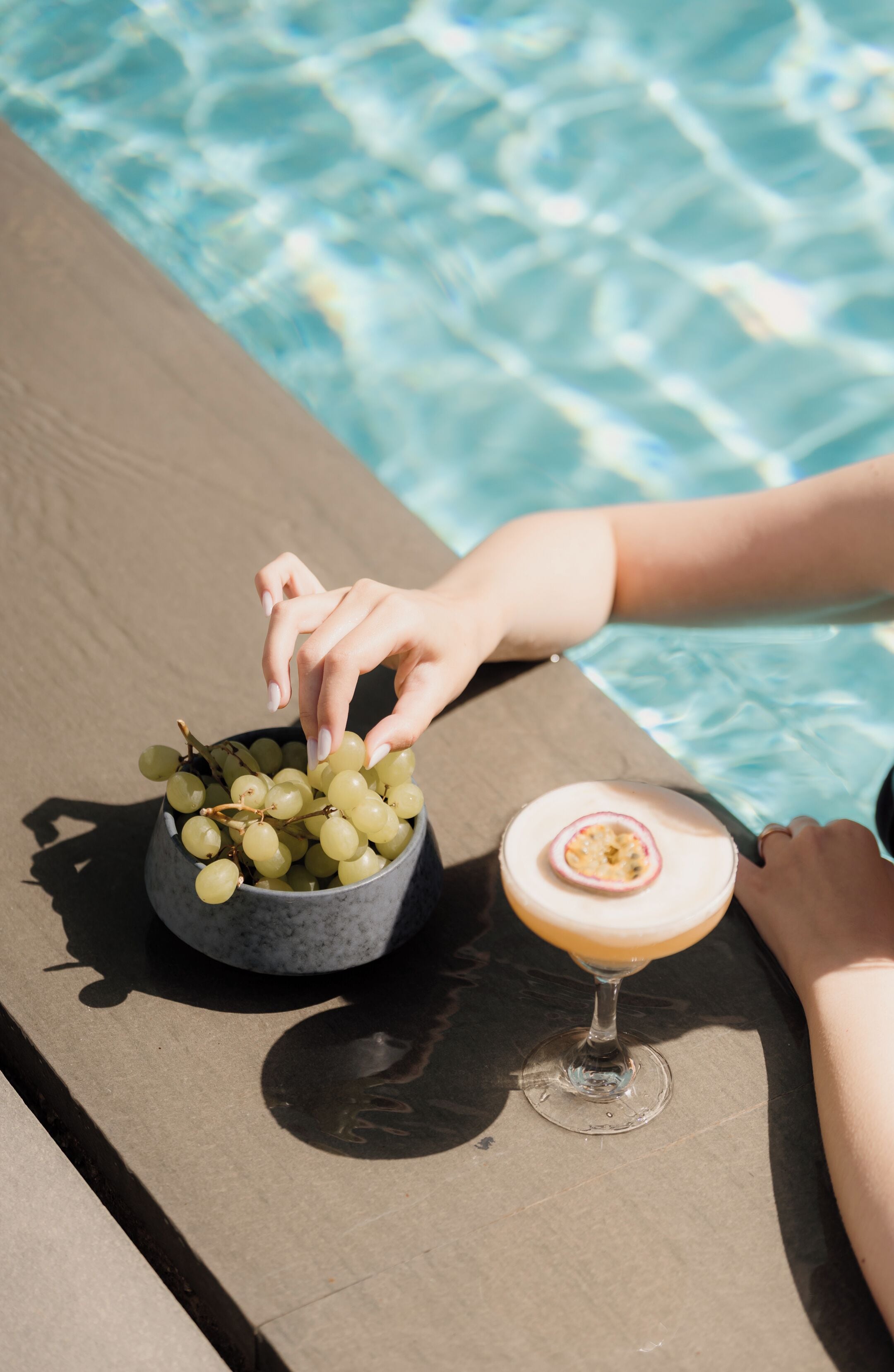 A poolside setting with a bowl of grapes and a cocktail glass.
