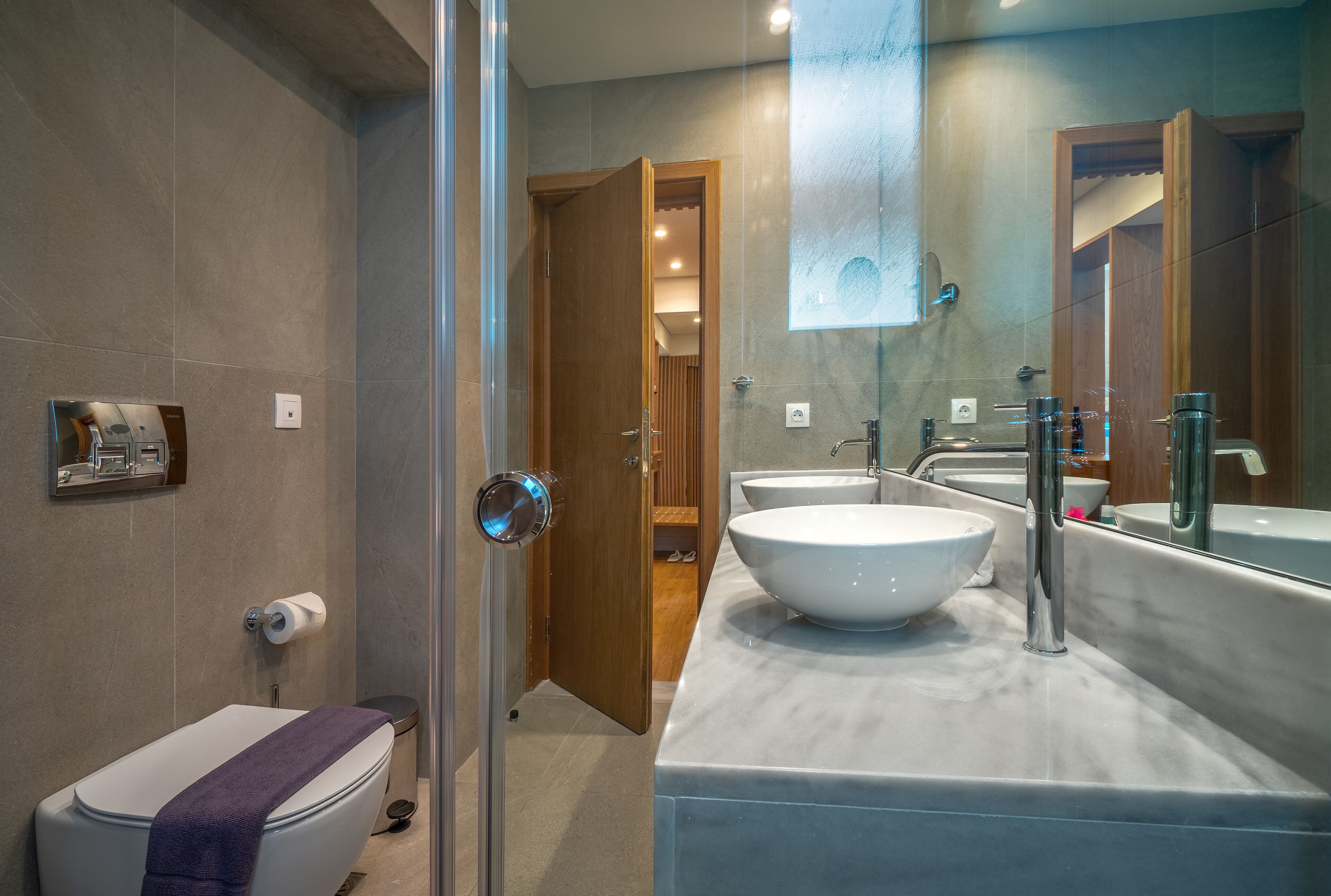 Une salle de bain moderne dotée d’une douche à parois de verre, de toilettes et d’un meuble-lavabo avec un grand évier et un miroir.
