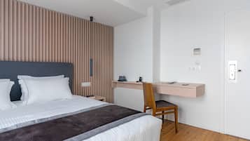 A modern hotel room with a large bed, a wooden slat wall, a desk with a chair, and a white door.