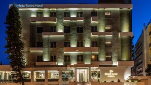 Exterior del Hotel Glyfada Riviera, con un diseño moderno, varios balcones y una entrada bien iluminada.