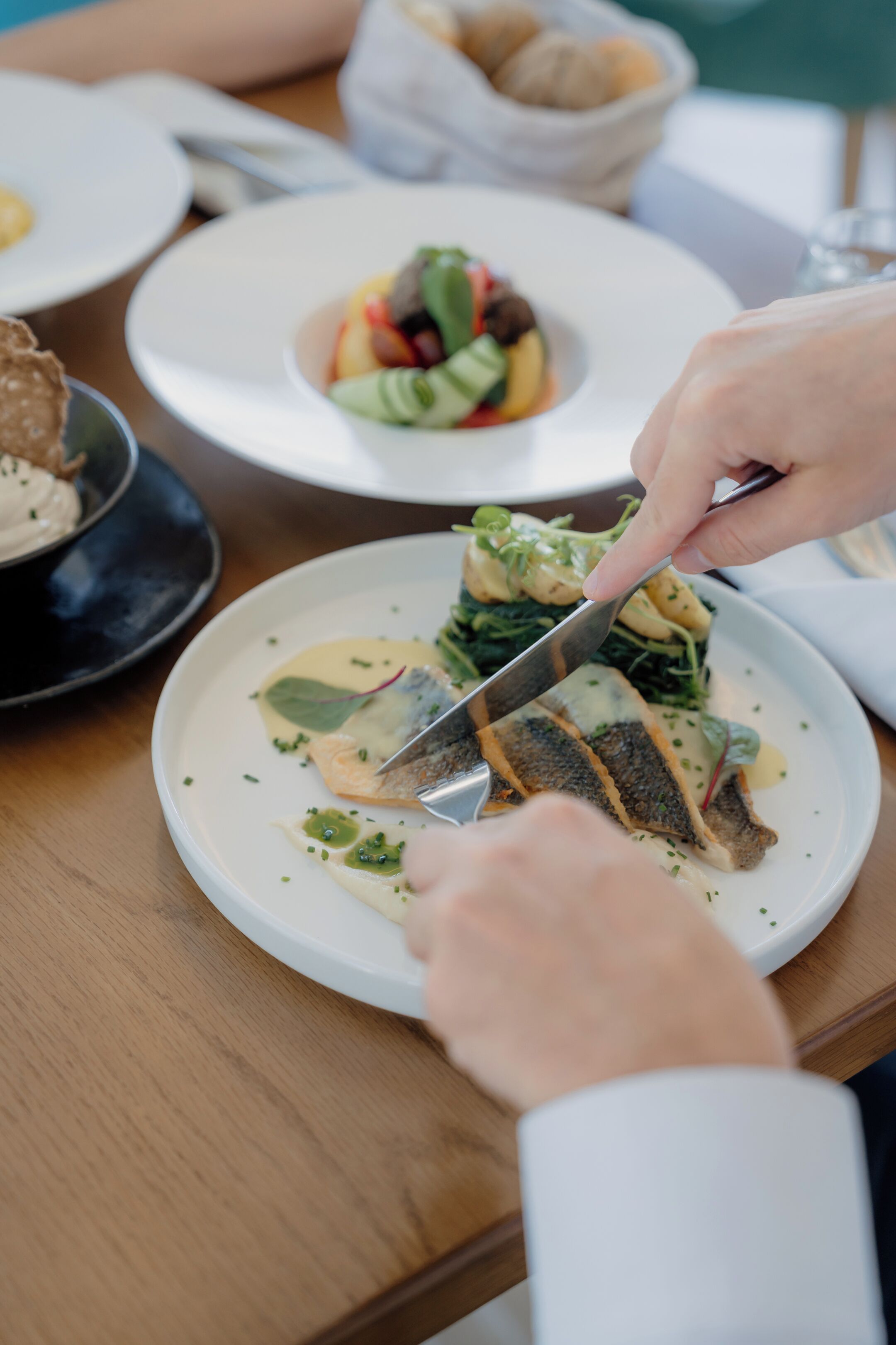 Uma pessoa corta um prato de peixe em um prato branco com um garfo.