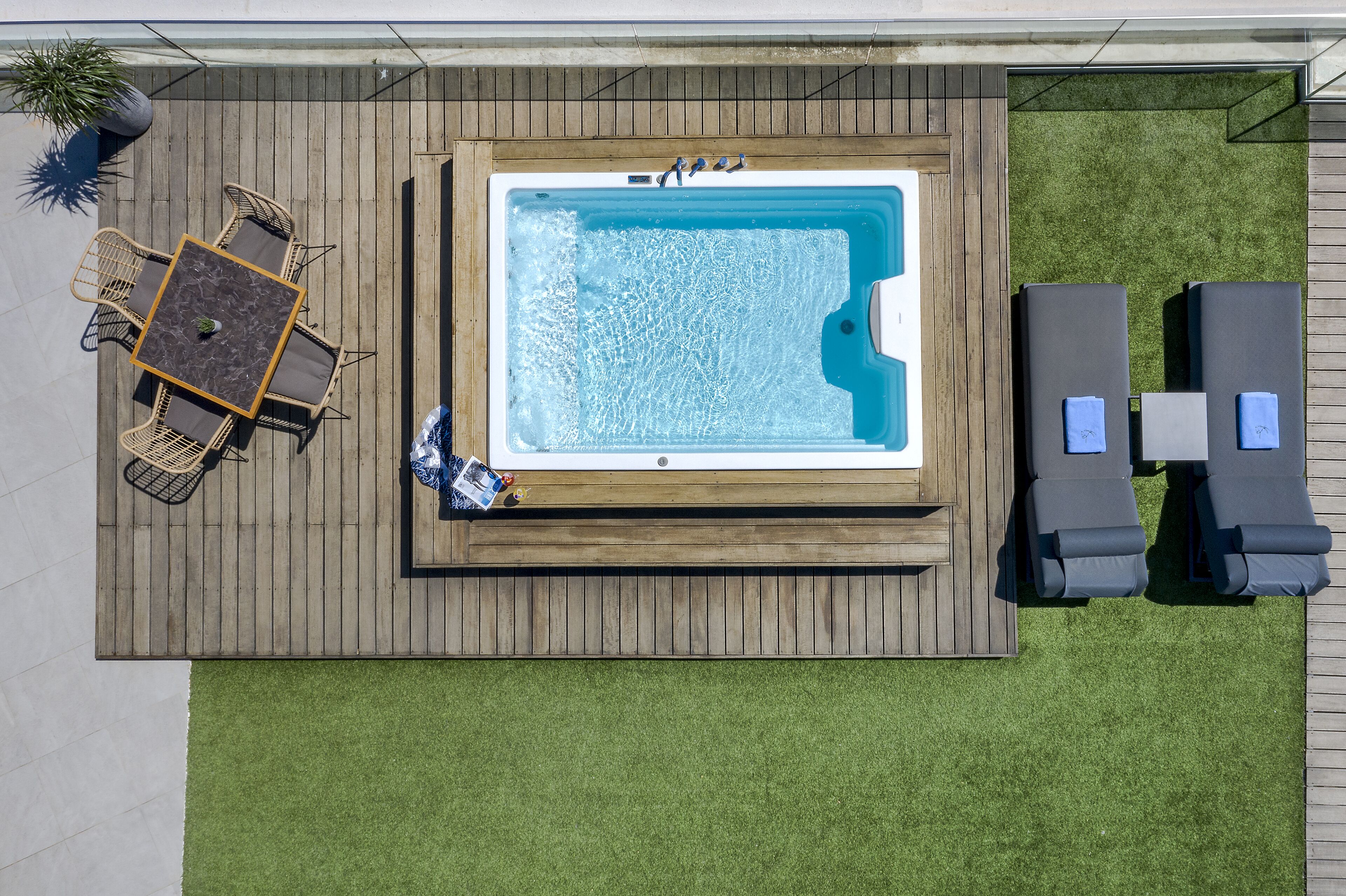 A hot tub surrounded by lounge chairs and a table with chairs on a wooden deck.