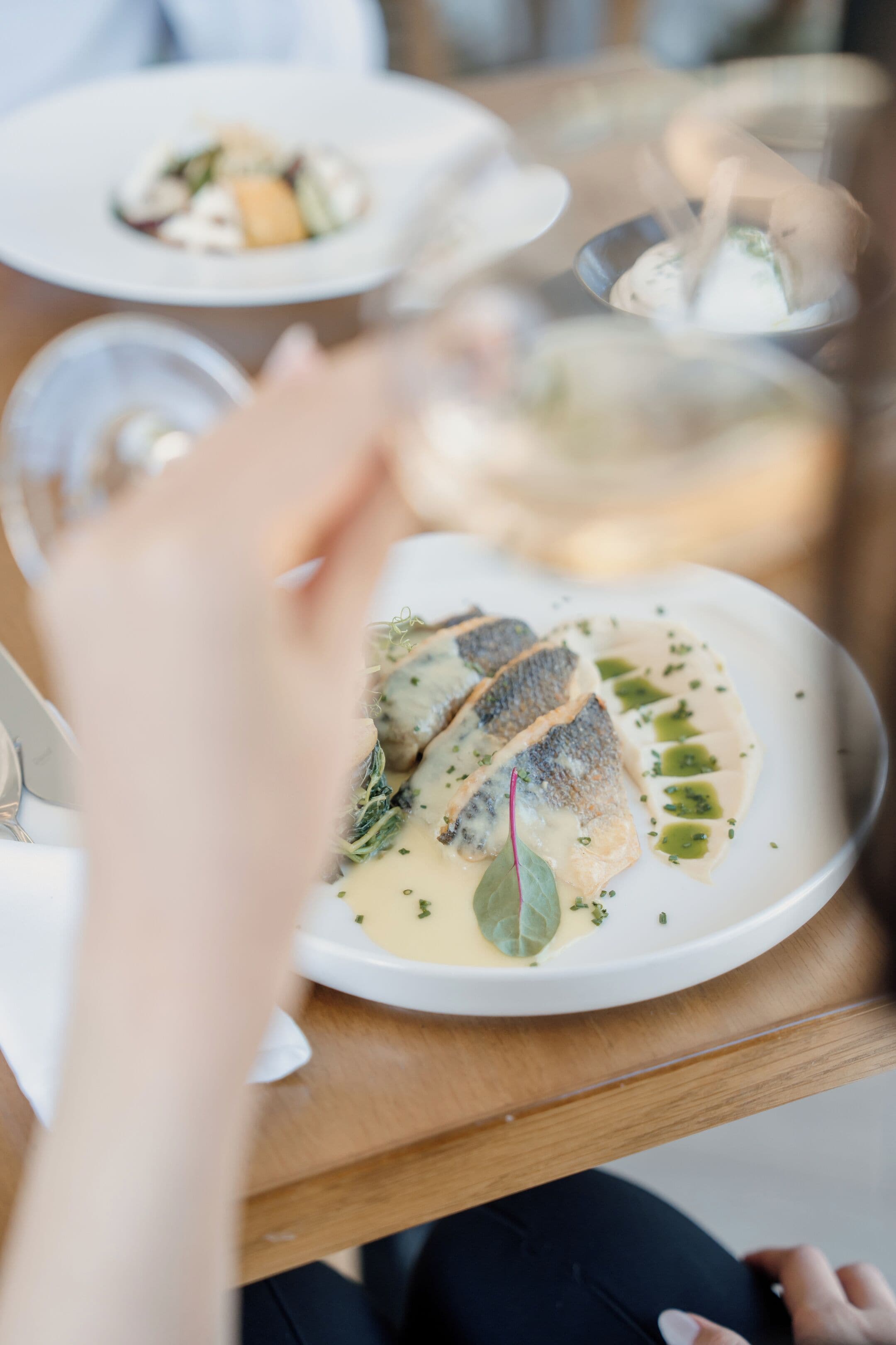 A dining table with plates of food and a glass of white wine.