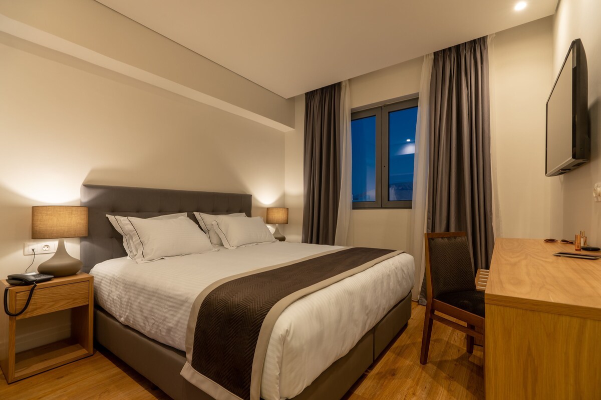 Una habitación de hotel con cama, lámparas de noche, escritorio y televisión.