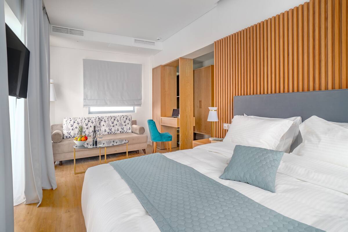 A modern hotel room with a large bed, a desk, a sofa, and a wooden accent wall.