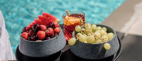 Een dienblad met schalen vol fruit en een drankje bij een zwembad.