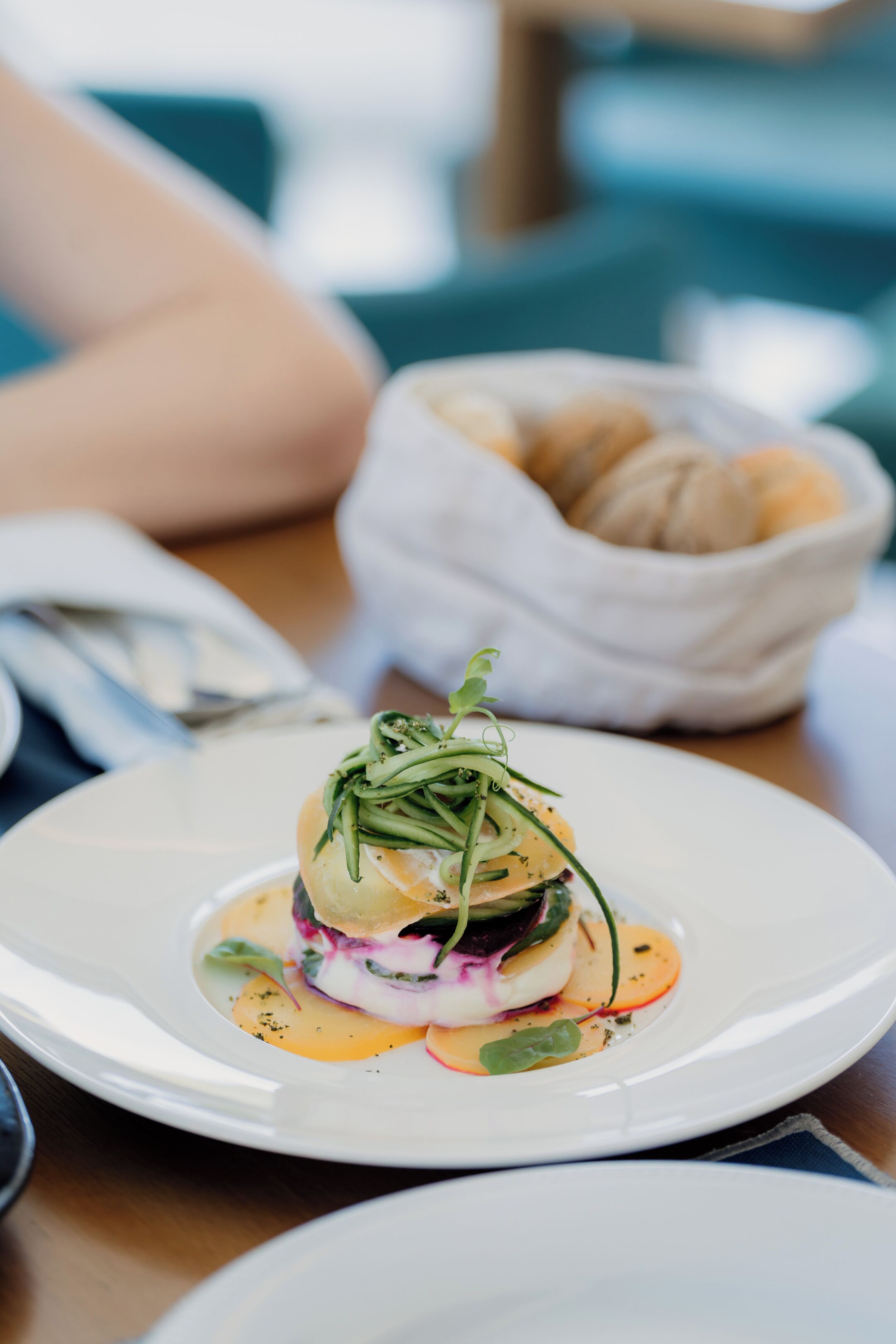 A white plate with a layered dish, a basket of bread, and a blurred background.