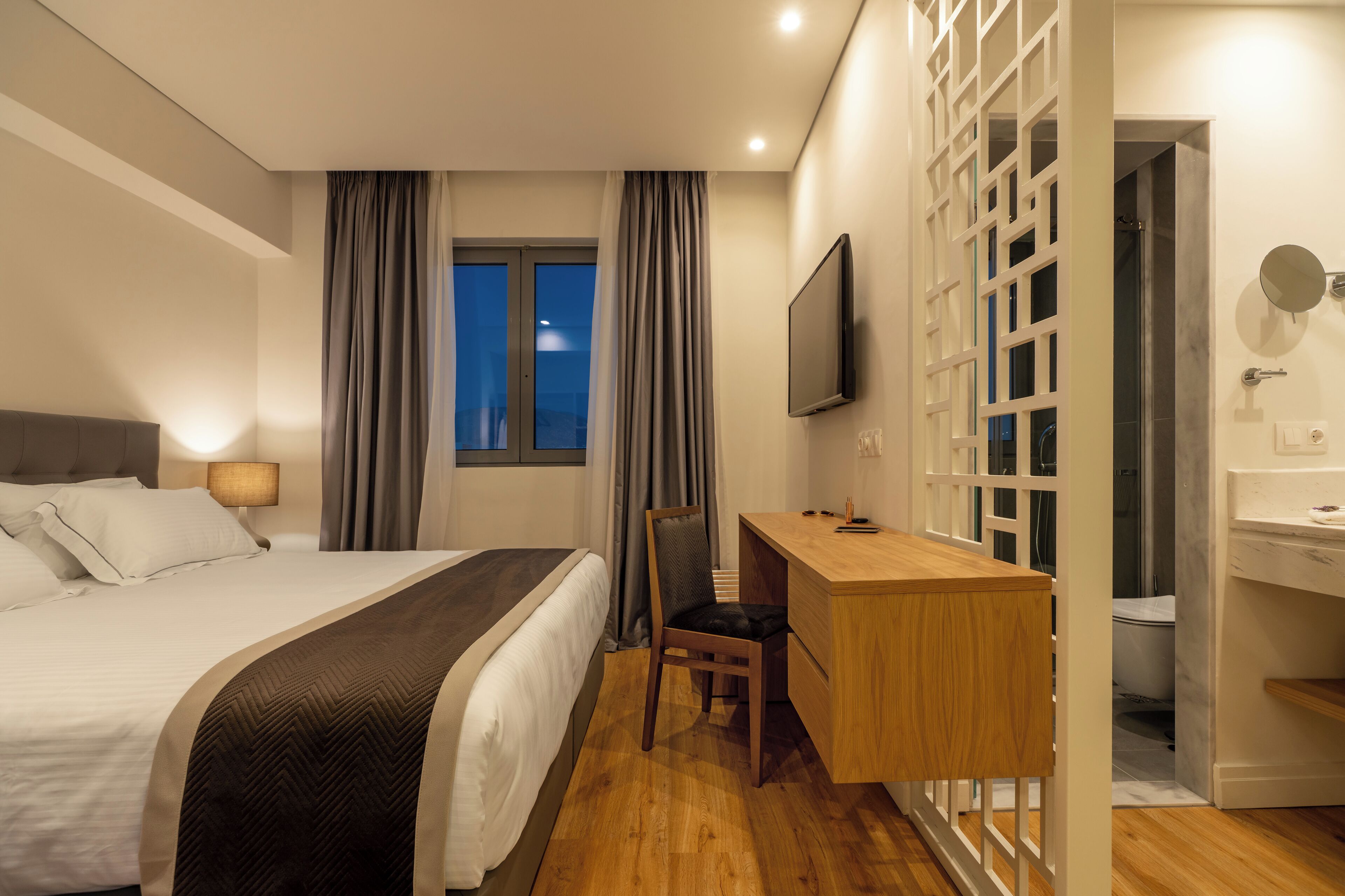 Habitació d'hotel amb llit, escriptori, cadira, televisió i bany.
