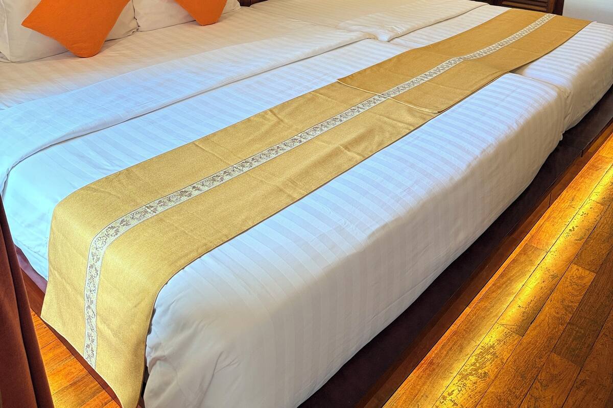 A large bed with white and orange pillows, a wooden headboard, and a decorative runner. There are two framed pictures on the wall above the bed.