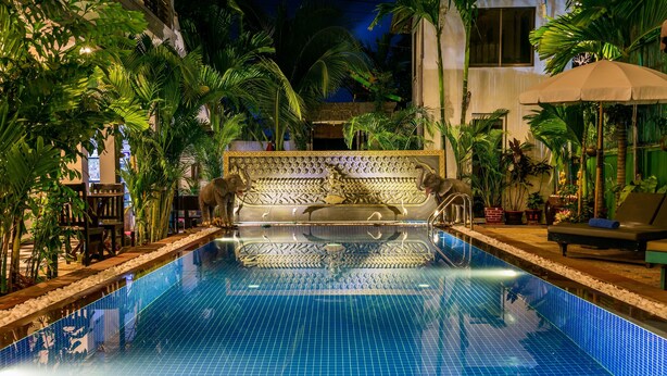 A pool with tiled flooring, surrounded by palm trees and a decorative bench.