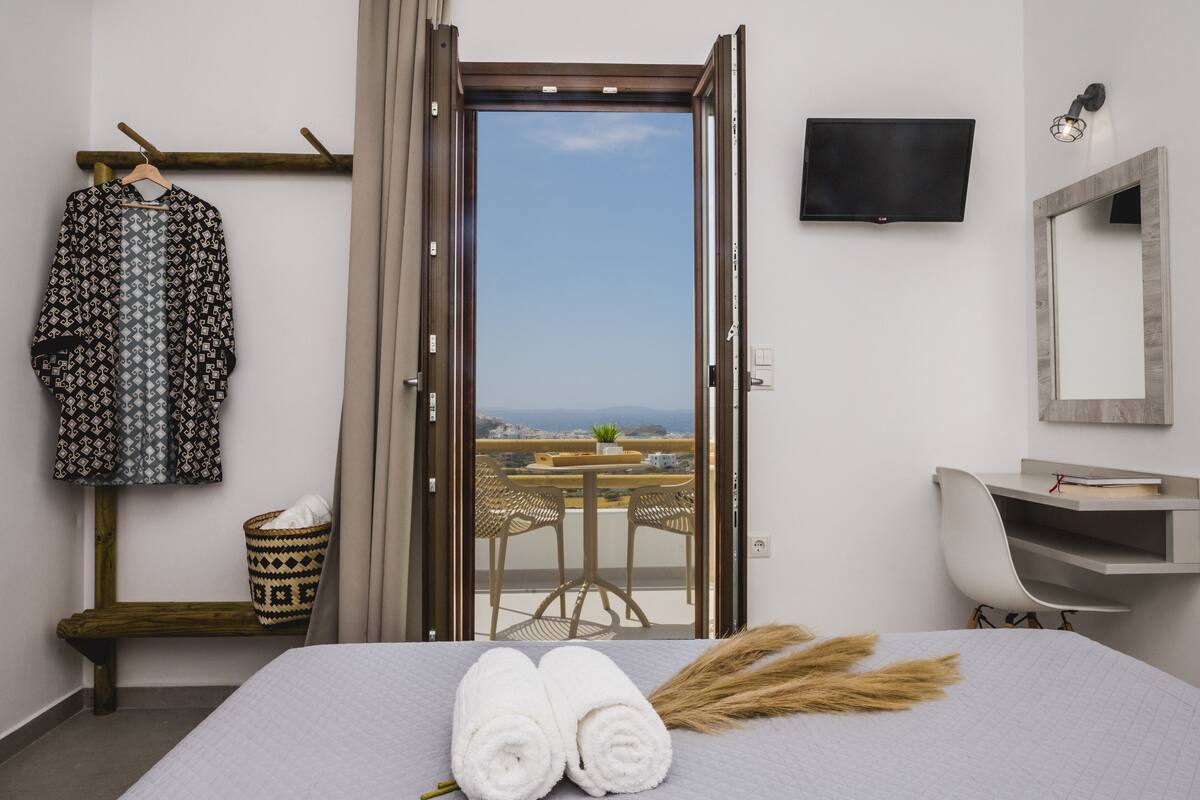 Habitación de hotel con cama, televisión, escritorio y balcón con vistas.