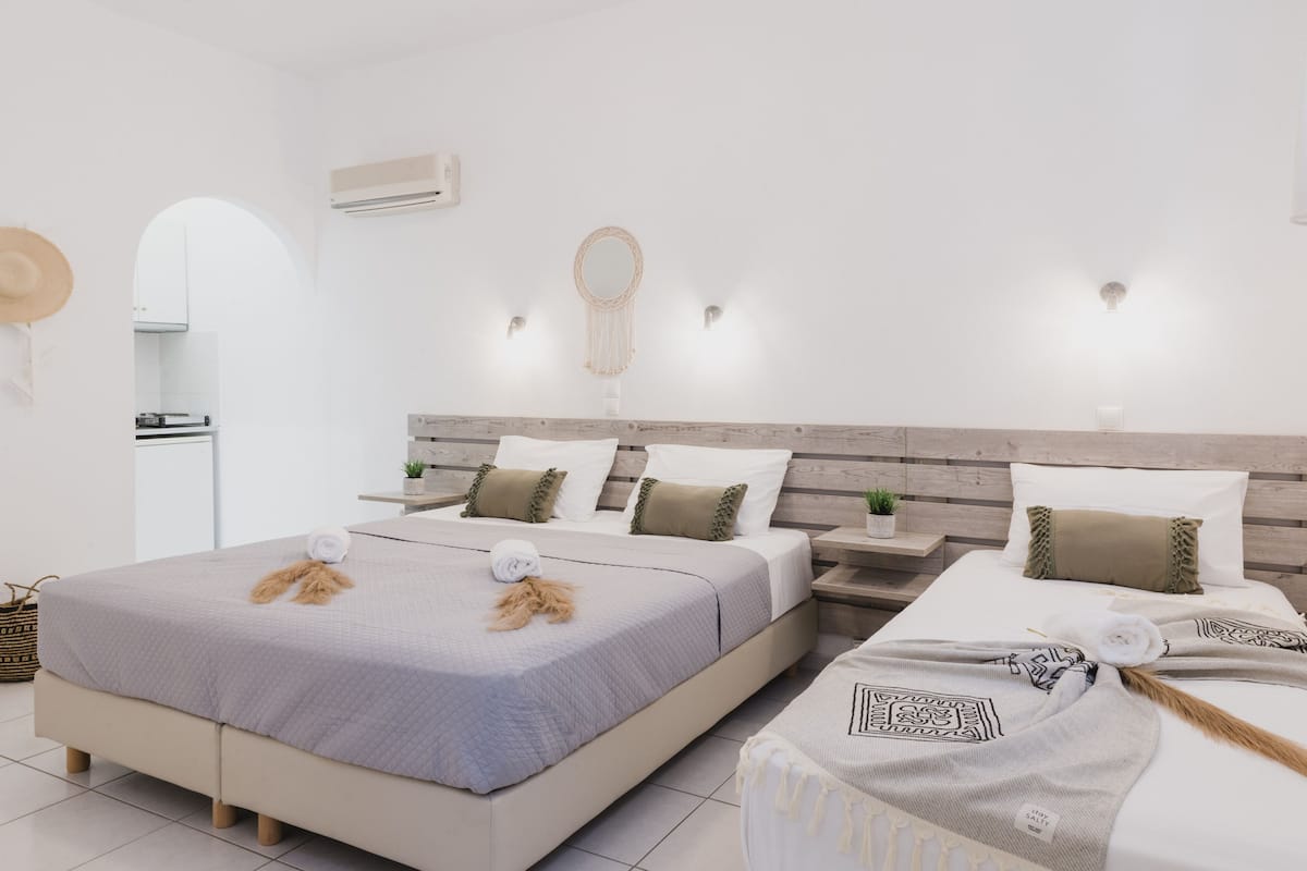 Una habitación de hotel moderna con una cama grande, una mesita de noche, una planta pequeña en maceta y un aire acondicionado de pared.